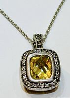 Close-up of pendant showing faceted lemon citrine center and small clear stones around it.