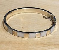 Silver bangle with alternating gold-tone and mother of pearl inlays, laid flat showing full circle and detail.