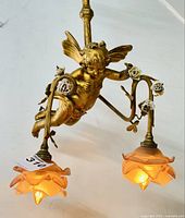 Close-up view of gilded cast bronze cherub and two peach-colored art glass shades