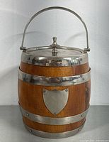 Front view of antique oak barrel biscuit container with silver plated handle, lid and trim showing wood grain and decorative shield plate.