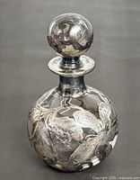 Full view of the clear glass perfume bottle with silver overlay design and round stopper