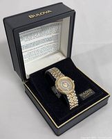 Watch displayed on black Bulova presentation box cushion with lid open, showing logo and printed warranty insert.