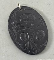 Front view of oval argillite pendant showing carved Raven design in Haida style.