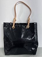 Front view of black patent leather Michael Kors tote bag with embossed MK logo pattern and tan straps.