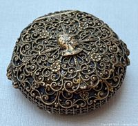 Top view of the small round brass pill box showing the ornate filigree design and the central knight head bust.