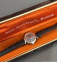 Photo showing vintage Bulova Mini Accutron watch resting inside original orange and brown presentation case with branded interior lining.