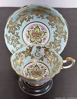 Close-up top-down view of the teacup inside the saucer showing the crown emblem and floral details with gold leaf accents.
