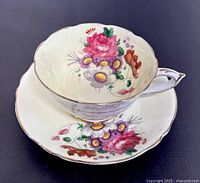 A side angle showing the teacup nestled inside the matching saucer. Both items have colorful floral decorations and gold trim.