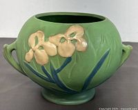 Front angle showing floral design in beige and blue on matte green background with ornate handles.