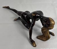 Full side view of the bronze nude woman sculpture in crawling pose highlighting elongated form and gold accents on hair, hands, and feet.