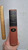 Spine of the hardcover book showing title The Complete Tales and Poems of Edgar Allan Poe Modern Library with ruler for scale