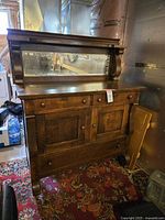 Front view showing two small drawers on top, two cabinet doors in the middle, and a lower drawer. Beveled mirror attached to back with carved wooden braces. Solid wood with aged patina and visible wood grain.
