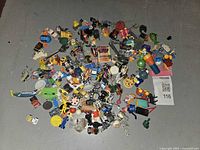 Overhead photo showing diverse collection of approximately 60 miniature toys including cars, figurines, tools, and novelty items.
