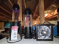 Three lamps side by side on shelf: Kenart Spiral Ball Lamp at left, Rocket Tornado Lava Lamp center, square strobe light at right.