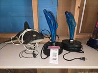 Shelf view showing glitter whale lamp coiled cord and two dolphin plasma lamps with power cords