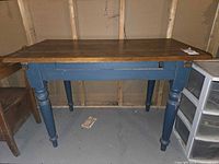 Front angled view of antique farmhouse table showing grainy pine wood top and navy blue base with turned legs.