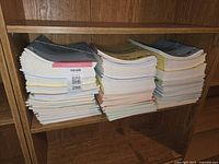 Stacks of new lined exercise books in multiple pastel colors on a wooden shelf showing quantity and condition.