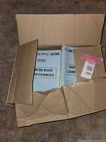 Open cardboard box showing stacks of blue-covered exercise books labeled 'Exercise Book Cahier d'Exercice' from FIERRO brand.