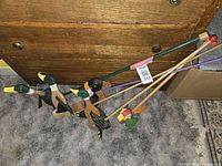 Photo of five wooden push-and-pull toys on a carpeted floor in front of a wooden dresser, showing three ducks, one penguin, and one parrot attached to colored sticks.