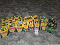 Photo showing arranged boxes of Crayola markers and colored pencils on carpet, with visible yellow and green packaging and product variety.