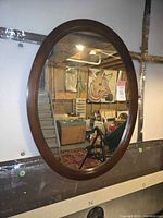 Front view of the oval mirror hanging on a wall reflecting a basement room with storage and art.