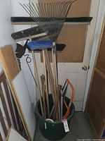 Full view of green bucket filled with garden tools leaning against door in narrow room