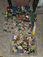 Top-down photo showing all farm toys spread out including tractors, trucks, numerous animals, and a container with farm equipment pieces.