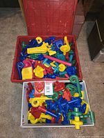 Wide view showing two large containers filled with assorted colorful marble run assembly pieces including tubes, ramps, funnels, and connectors.