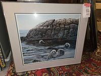Framed artwork print showing full image of sea otters in water near a rocky shore with matting and frame.