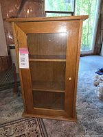 Front view of small pine cabinet with glass door, showing two interior shelves and missing door knob.