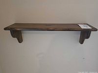 Frontal side view of the wooden wall shelf mounted on a wall, showing the full length and finished surface.