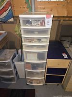 Full view of tall white plastic storage unit with seven drawers, some translucent, some opaque, showing contents inside and storage on top