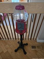 Full front view of the tall vintage metal gumball machine, showing its height, black base, red body, and clear glass globe.