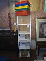 Tall white shelf unit with plastic bins on top and stacks of paper inside shelves, surrounded by other furniture items.