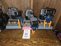 Three Armatron robotic arm toys displayed on a wooden surface with a white MaSold auction card in front