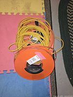 Top view of three yellow extension cords coiled on orange plastic reels on foam mat and floor.