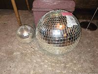 Photo showing both the small and large disco balls side by side on carpeted floor, highlighting their size difference and reflective mirror tiles.