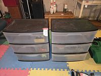 Two black-top plastic storage units with translucent drawers set on colored foam floor tiles, filled with hardware.