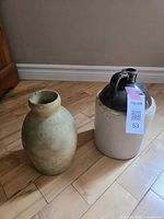 Photo of both pottery items showing crock jug with two handles and dark brown top, and beige pottery vase