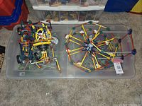 Two clear plastic bins containing partially assembled Knex models with colorful rods and connectors, placed on carpet.