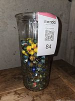 Side view of a clear ribbed glass vase approximately 3/4 full of mixed vintage marbles.