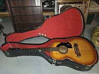 Open guitar case with the Framus Gaucho acoustic guitar inside showing the front body and neck with sunburst finish and black pickguard.