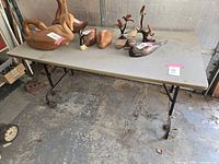 Full front view of the folding table with wooden top and black metal legs in a garage setting with wooden decor items on top.