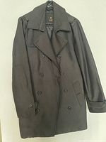 Front view of classic black double-breasted coat with six buttons and two slanted front pockets, size small.