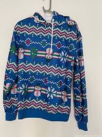 Front view of blue Christmas hoodie with snowmen, zigzag and tree patterns, showing full front and hood with drawstrings.