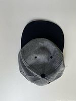 Top view of the grey fabric cap with black brim showing the crown and button.