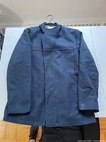 Front view of a men's solid navy blue coat, medium size, with zip and button closure, showing the structured collar and overlap front design.