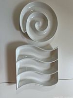 Photo showing white round ceramic serving dish with spiral design and another rectangular dish with three wavy sections on a flat surface.