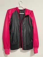 Front view of the women's Nike hooded jacket, showing black body with bright pink sleeves and hood, full front zipper, and zippered pockets.