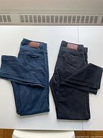 Two pairs of folded pants, one blue and one black, laid out on a flat surface showing front and back angles.
